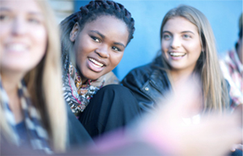 Weiblich gelesene junge Menschen schauen lachend auf einen Punkt neben der Kamera